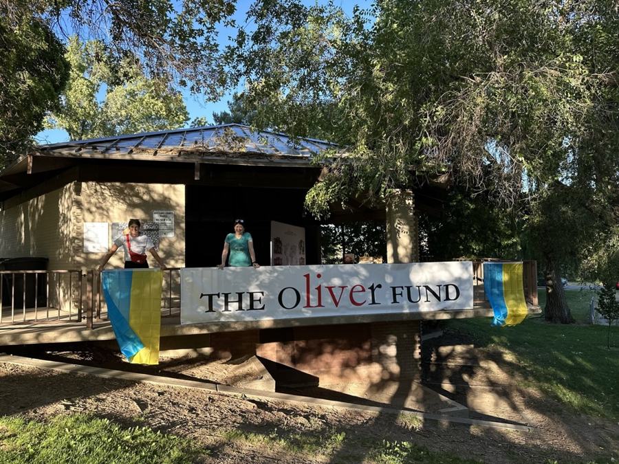 Two volunteers at a park pavilion draped with an Oliver Fund banner and Ukrainian flags