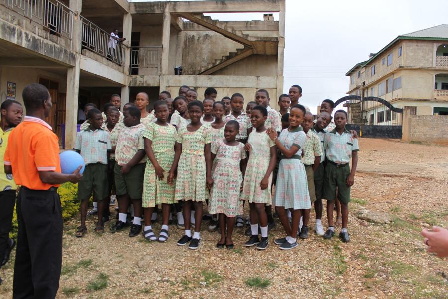 A large group of students in school uniforms poses with a ball