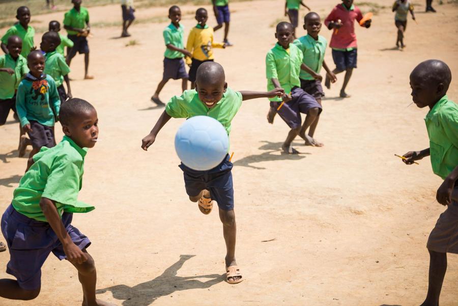 A boy chases a blue ball with classmates in green shirts